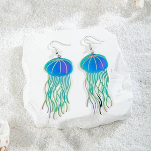 Iridescent jellyfish drop earrings with colorful metallic finish on white sand background