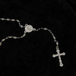 Detailed close-up of a silver cross pendant and religious medal on a link chain necklace
