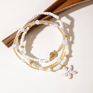 Detalle de tobilleras de playa con colgantes de concha dorada y estrella de mar blanca