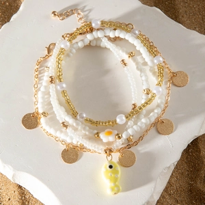 Detalle de tobillera bohemia de varias capas con lentejuelas doradas y dije de pez amarillo