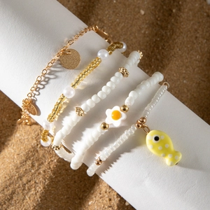 Detalle de set de 5 tobilleras bohemias con cuentas amarillas y dije de pez en la arena