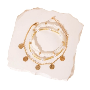 Set de tobilleras bohemias multicapa con colgantes dorados y perlas sobre piedra blanca