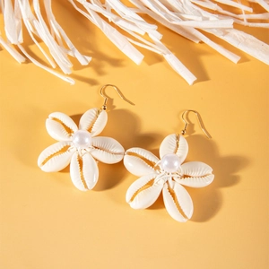 Vista macro de pendientes de flores de concha con perla blanca y ganchos dorados