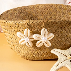 Detalle de pendientes de flores de concha hechos a mano con perla sobre un decorado de playa