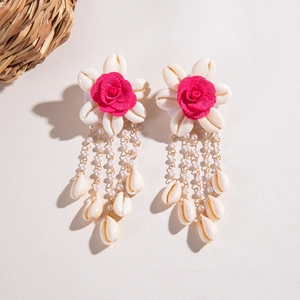 Detalle de pendientes bohemios de concha con rosas rojas y cadenas metálicas colgantes