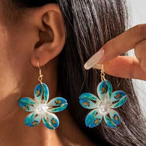 Detalle de pendientes de flores de nácar con pétalos azules y perla en una modelo