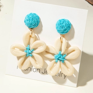 Detalle de pendientes de flores de concha hechos a mano con centro tejido en azul claro