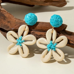 Detalle macro de pendientes bohemios hechos a mano con flores de concha y detalles tejidos