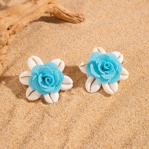 Detalle de pendientes de flores de concha hechos a mano con rosa azul sobre fondo de arena