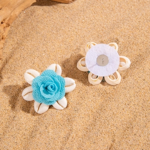 Detalle de broche de rosa de tela azul con conchas naturales sobre fondo de arena