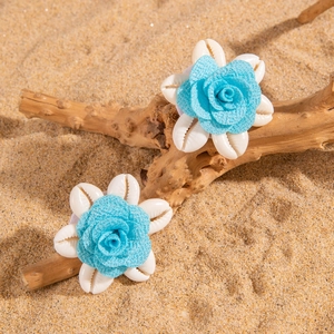 Detalle de coleteros playeros con rosas de tela azul cielo y conchas blancas en la arena