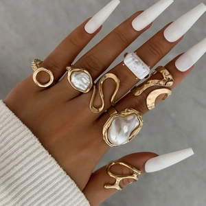 Detailed close-up of 7-piece gold geometric ring set with baroque pearl accents on hand