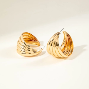 Macro detail of golden C-shaped hoop earrings with vertical ribbed texture and luxury finish