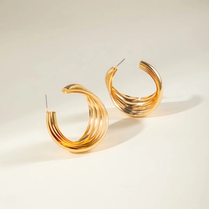 Macro shot of gold geometric C-shaped hoop earrings with a striped texture finish
