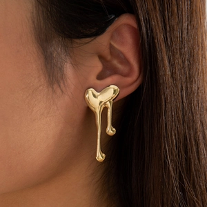 Close-up of golden geometric melted heart stud earrings worn on a female ear