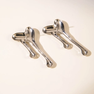 Macro view of liquid heart silver earrings with melting metallic texture on beige background