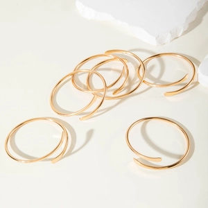 Eleganter goldener Spiral-Armreif mit flachen Enden auf minimalistischem Stein-Hintergrund