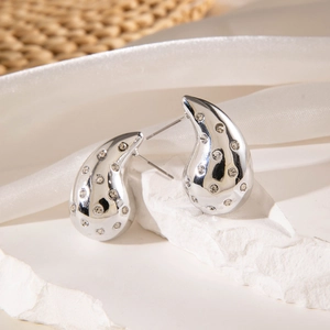 Detail of silver drop earrings with inlaid clear zircons on a white textured background