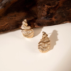 Detailed close-up of golden spiral earrings with textured vertical ridges on a rustic wood base