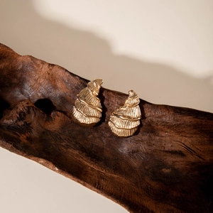 Close-up of golden geometric earrings with ribbed texture on a wooden prop background