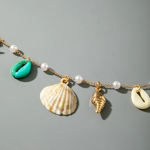 Macro view of gold beach body chain with sea shells, pearls and turquoise charms