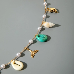 Detail of seashell beach body chain with gold pendants and white pearls on grey surface
