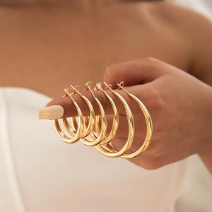 Close-up of triple gold hoop earrings set in various sizes held on fingers