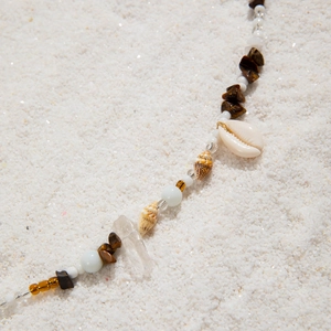 Detailed close-up of bohemian shell and bead waist chain with natural quartz on beach sand