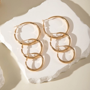 Three pairs of shiny gold hoop earrings in different sizes displayed on a stone tray