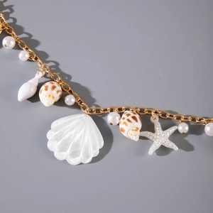 Close-up of beach body chain with white shells, starfish, and pearls on gold chain