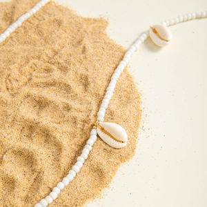 Close-up of beaded beach body chain with white sea shells on soft yellow sand