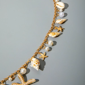 Macro detail of golden body chain with natural shells, starfish charms and white pearls