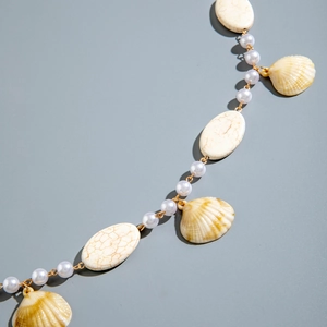Detailed close-up of beach style seashell pendant with textured beads and golden hardware