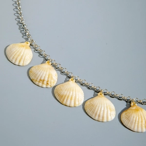 Close-up of five natural seashells hanging on a delicate silver metallic chain link