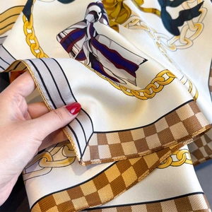 Macro shot of silk scarf detailing gold chain prints and brown checkered borders