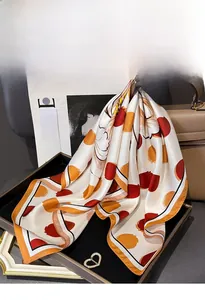 Detail of silk twill square scarf with orange leaf print draped over a luxury handbag
