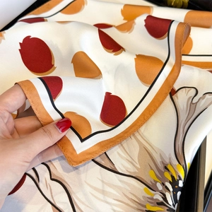 Detailed view of hand-rolled edges on a floral silk scarf with orange and black contrast