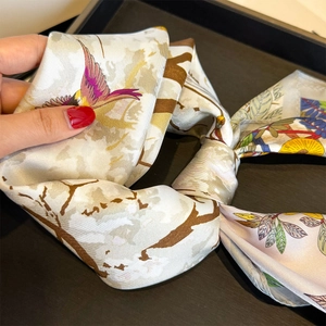 Detailed macro view of high-end silk scarf featuring floral and bird prints on beige fabric