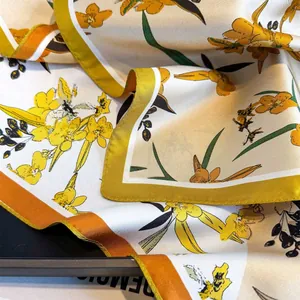 Close-up of vintage silk scarf featuring yellow floral patterns on a dark tray