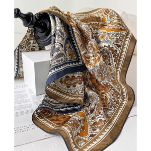 Fashionable paisley silk scarf in brown and navy tones folded on a white geometric stand