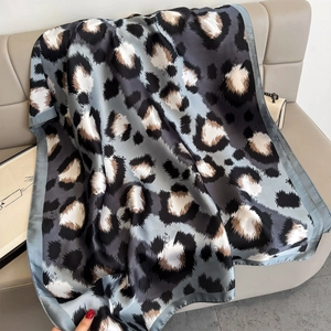 Blau-grauer Seidenschal mit Leopardenmuster und Glanz-Finish auf einem beigen Sofa