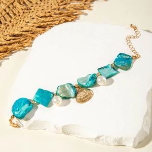 Macro view of ocean style bracelet with green ore beads, pearls and golden shell pendant