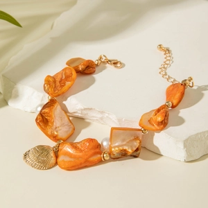 Macro view of ocean shell bracelet with pearls and golden scallop charm on white stone