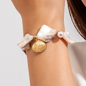 Detailed close-up of a gold scallop shell charm and baroque pearls on a beach style bracelet