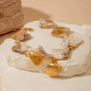 Detail of shell and pearl bracelet with golden scallop charm on a white stone slab