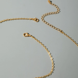 Détail d'une chaîne d'extension dorée avec fermoirs mousquetons et petite boule polie
