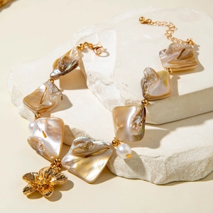 Macro detail of natural mother-of-pearl beads and a gold floral charm on the bracelet