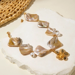 Detail of seashell bracelet with irregular pearl and golden flower charm on stone