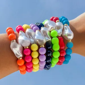 Detailed view of 8 colorful beaded bracelets with baroque pearls worn against a blue sky