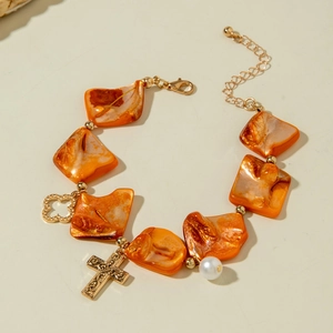 Detail of orange beaded bracelet featuring golden cross, clover, and pearl charms